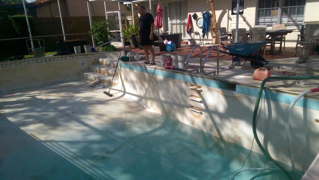 A person stands by an empty backyard swimming pool undergoing maintenance, with construction equipment and tools nearby.