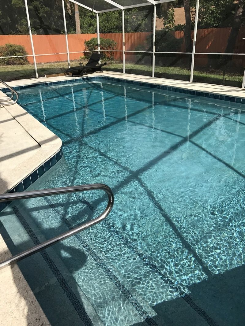 A clear rectangular swimming pool enclosed by a screen cage with a light-colored deck.