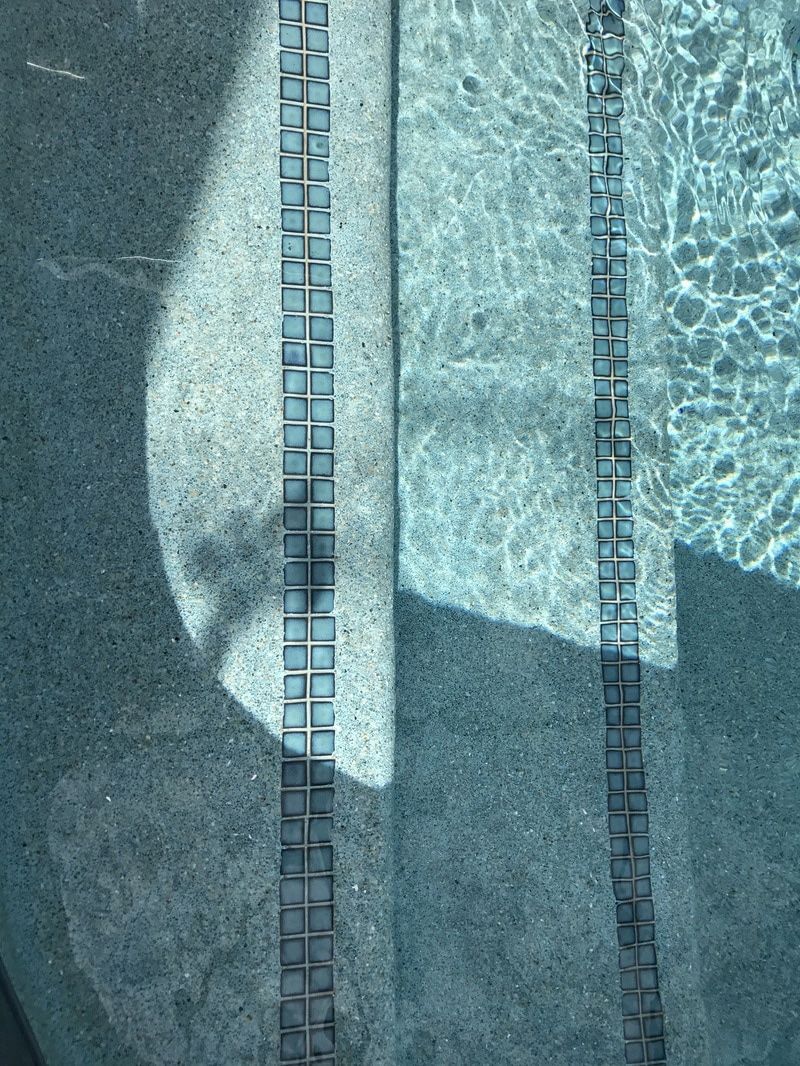High-angle view of two rows of dark square tiles embedded into the steps of a blue swimming pool.