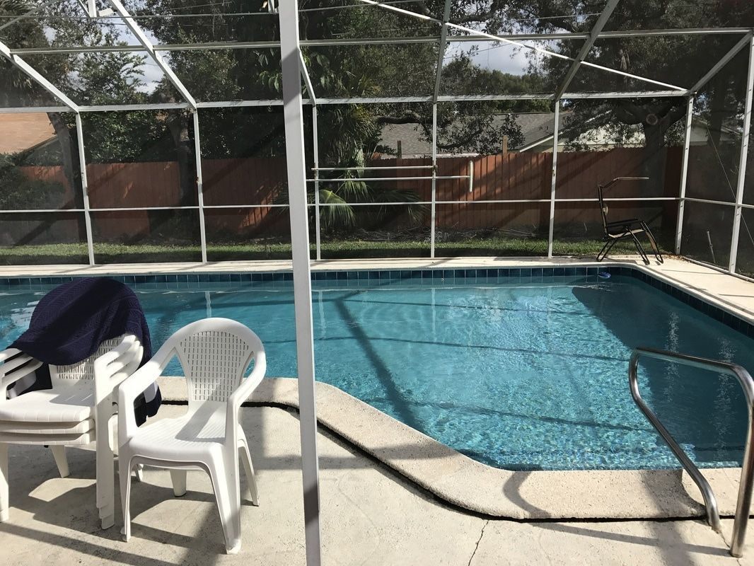 A swimming pool inside a screened-in lanai with white patio chairs on the concrete deck.
