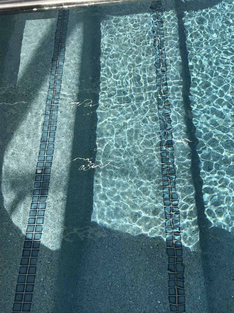 A swimming pool floor with dark tile lane markings and shifting light patterns caused by water surface movement.
