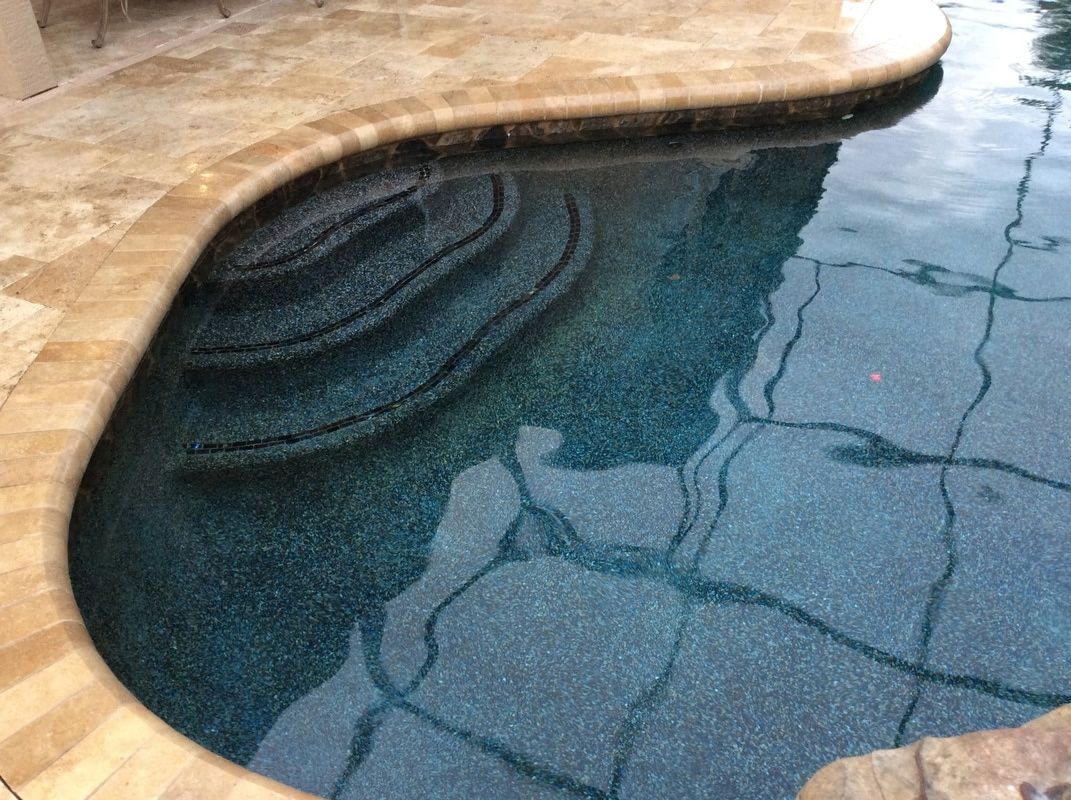 Curved swimming pool steps with dark blue pebble finish, bordered by beige stone coping.