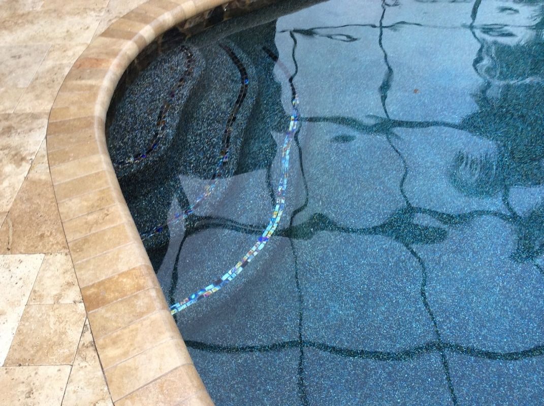A high-angle view of a curved pool edge with stone coping and dark blue textured pool steps leading into the water.