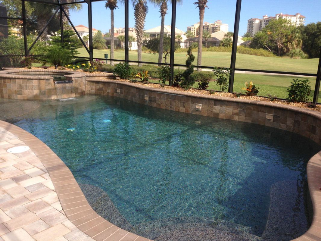 A backyard swimming pool with a raised hot tub and waterfall, enclosed by a screen, overlooking a golf course.