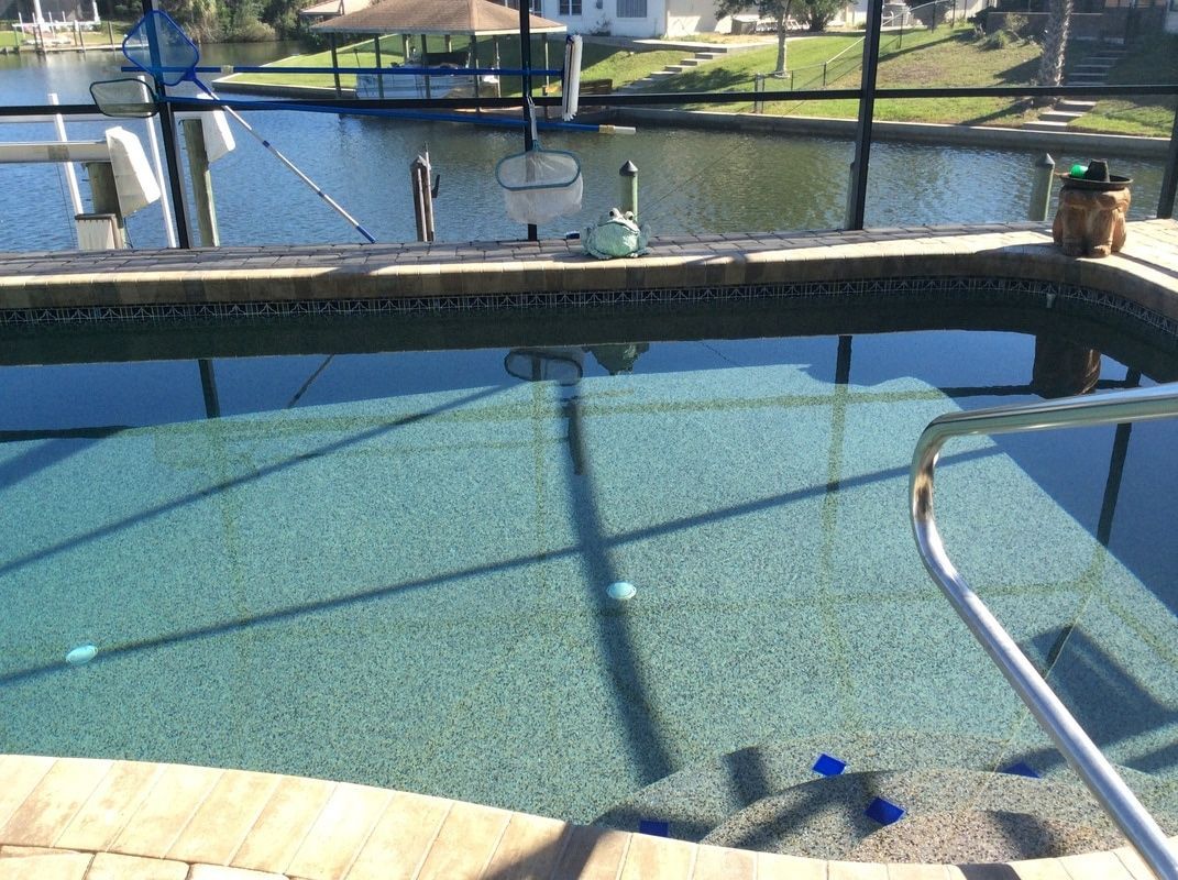 A clear swimming pool with steps, viewed through a screened enclosure overlooking a calm canal with a small boat dock.