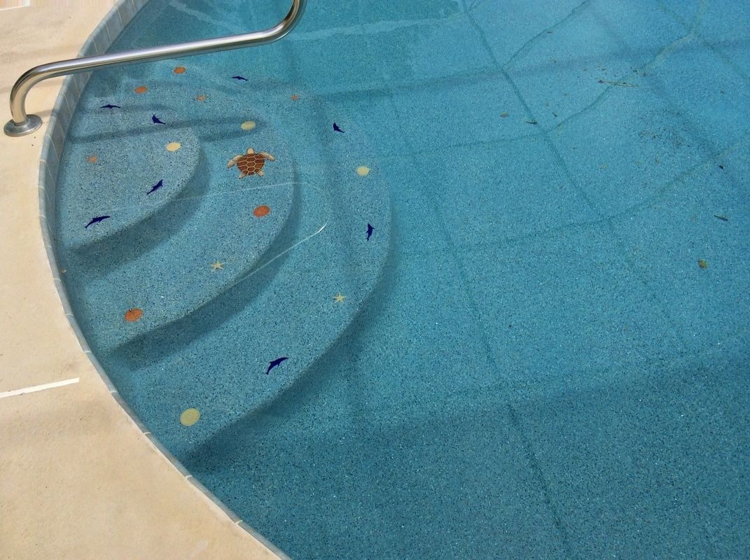 Top view of rounded blue swimming pool steps with a metal handrail and decorative sea life tile accents.