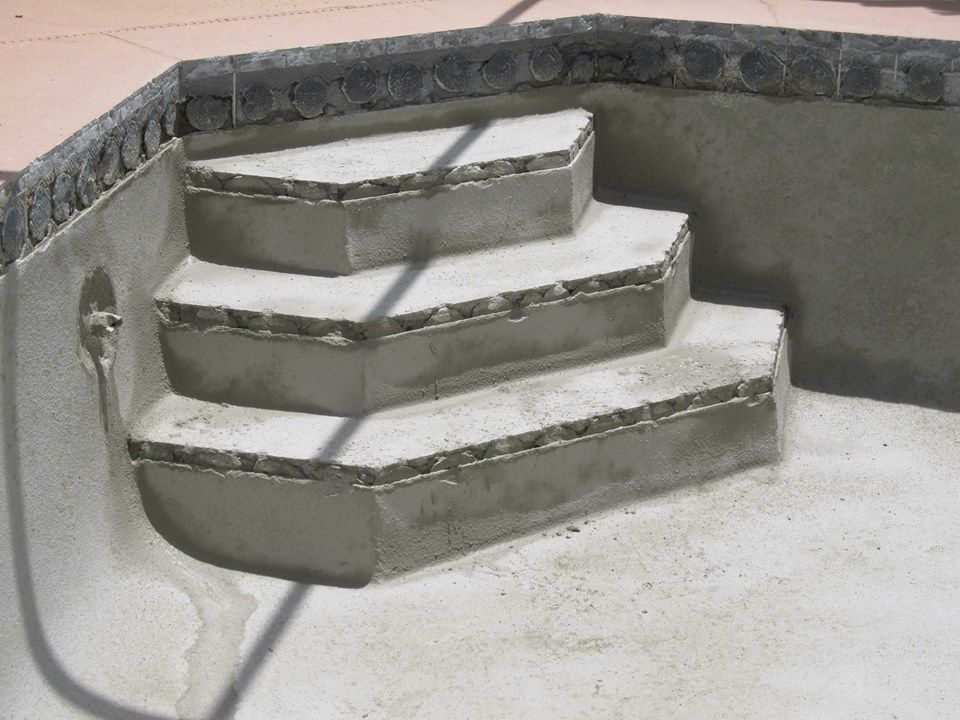 Concrete steps in a swimming pool under construction, showing rough grey masonry with a curved edge.