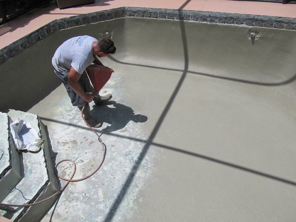 A worker using a power tool to smooth the surface of an empty, light gray concrete swimming pool.