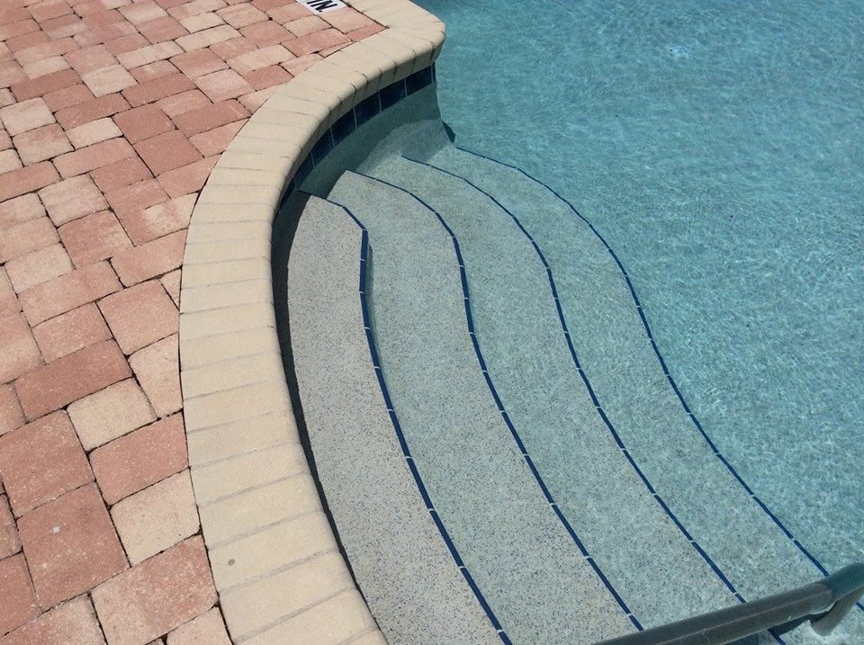 Curved swimming pool steps with light-colored coping and stone pavers on the deck.