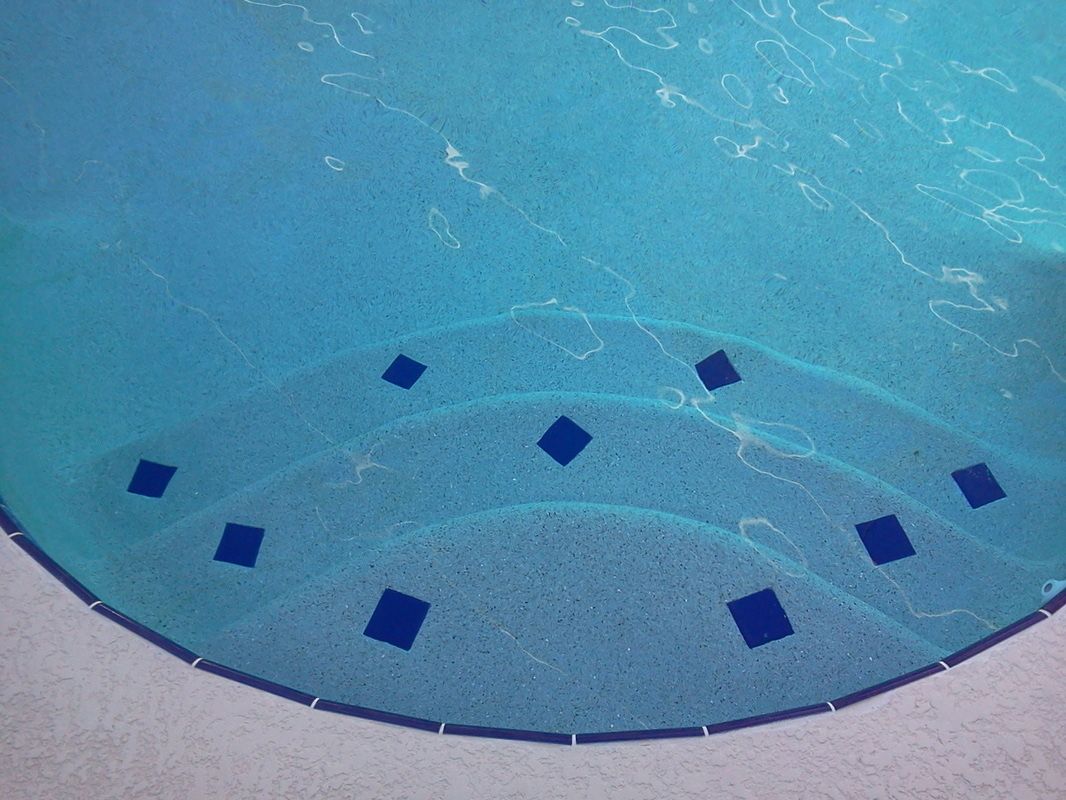Curved swimming pool steps with dark blue square tile accents under clear blue water.