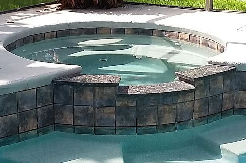 An elevated, round tiled spa attached to a swimming pool, featuring dark-toned masonry and light-colored coping.