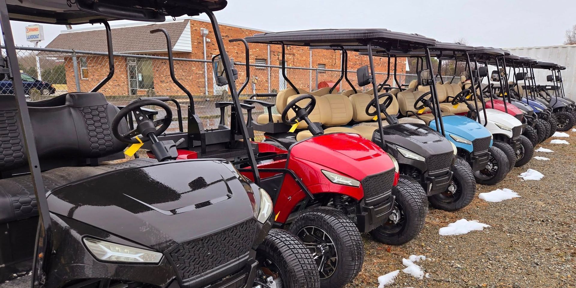 A row of golf carts are parked in a gravel lot.