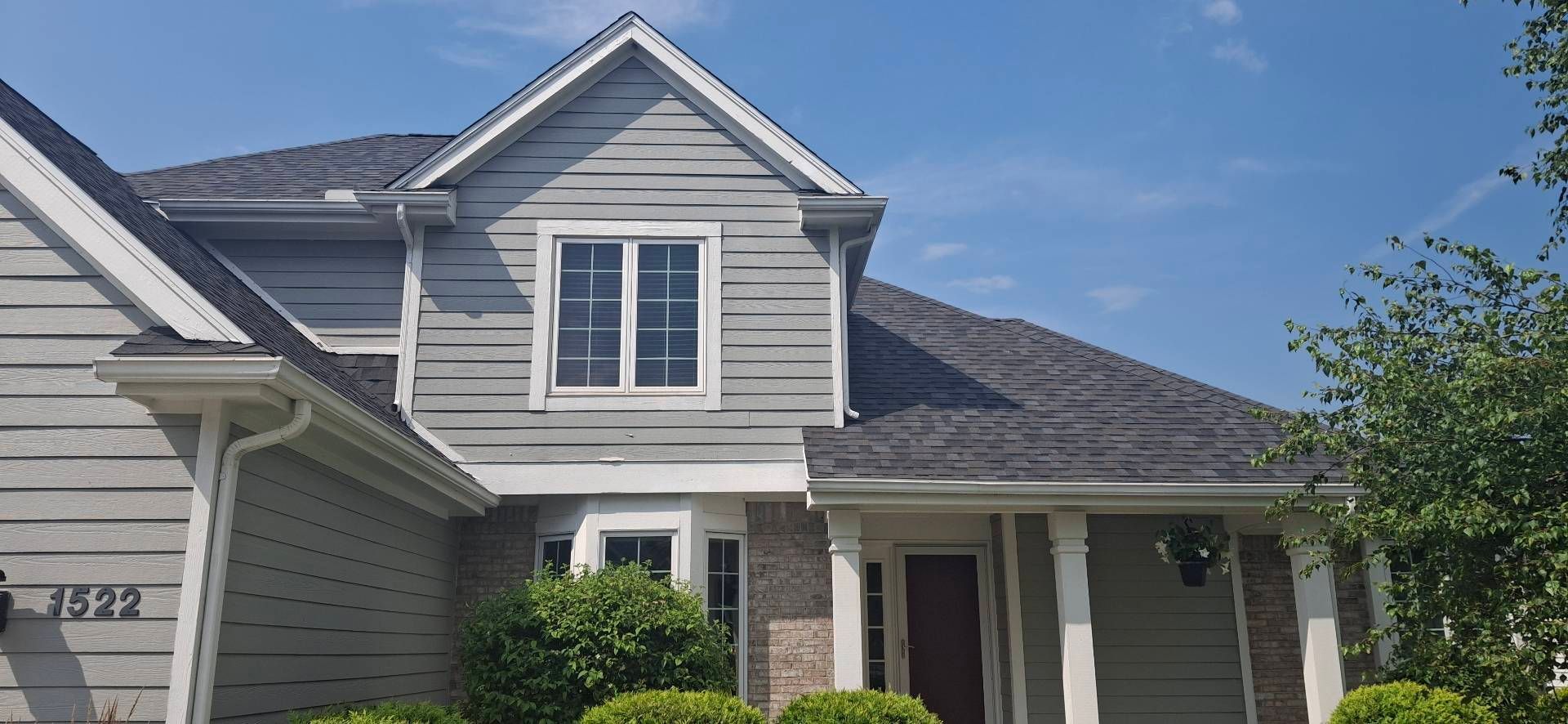 Gray house with dark gray roof, blue sky, and green bushes.
