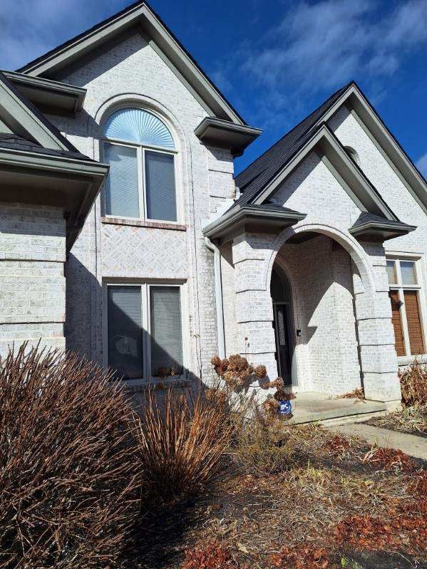 Brick house exterior with arched entry, gabled roof, and leaf-covered front yard under blue sky