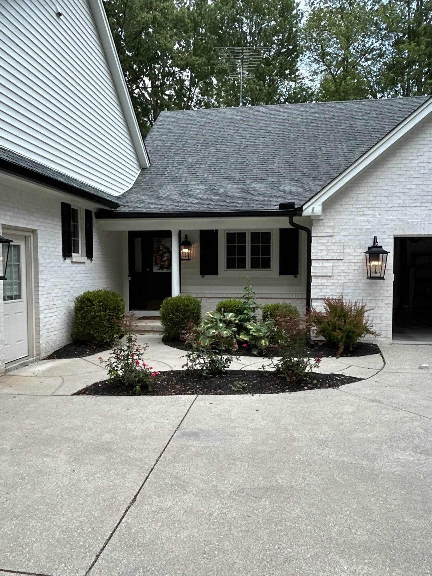 Residential driveway and front entrance with white siding, gray roof, and small landscaped beds.