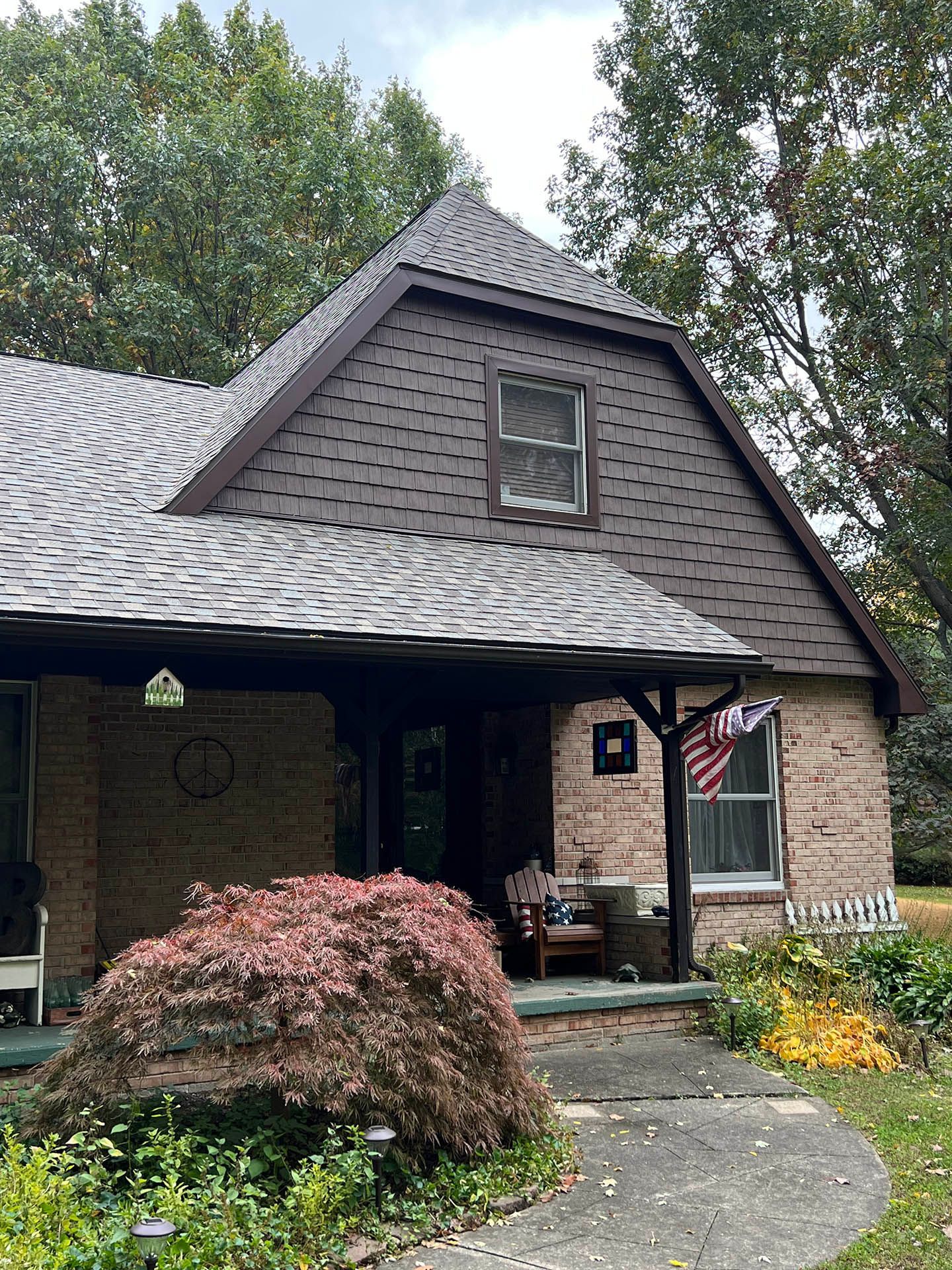 Brick house with dark shingled roof, front porch, and a curved walkway bordered by shrubs and flowers