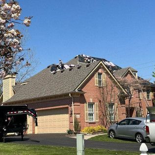 Suburban house with roofers working, parked cars, and a blooming tree in front yard