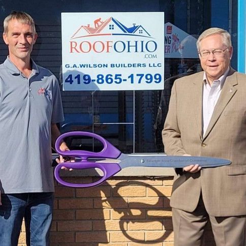 Two men holding oversized purple scissors in front of a roof repair business sign.