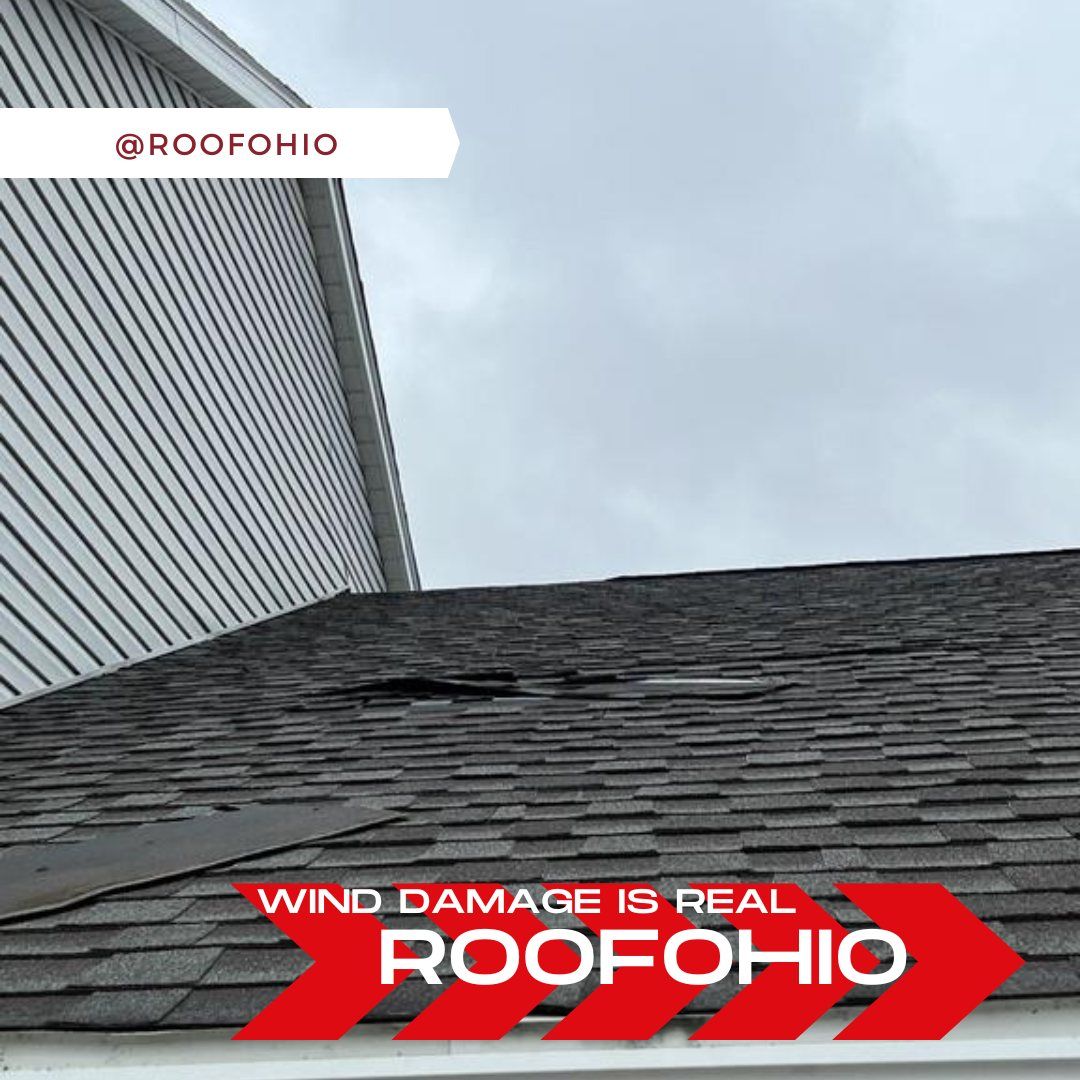 Roof shingles damaged by wind beside a house wall under a cloudy sky, with Roof Ohio logo.