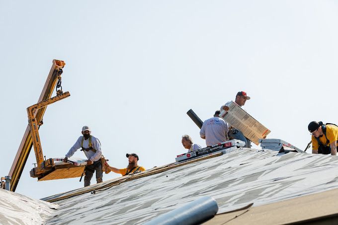 Workers on a rooftop installing metal panels with a boom lift against a clear sky