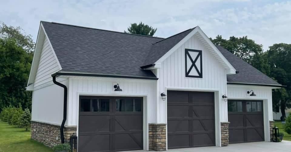 White three-bay garage with black doors, stone accents, and a dark roof on a grassy lot