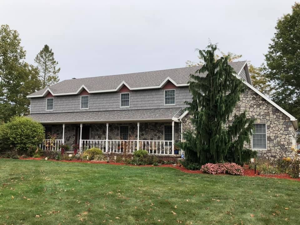 Stone house with gray roof, front porch, and landscaped lawn in a suburban yard