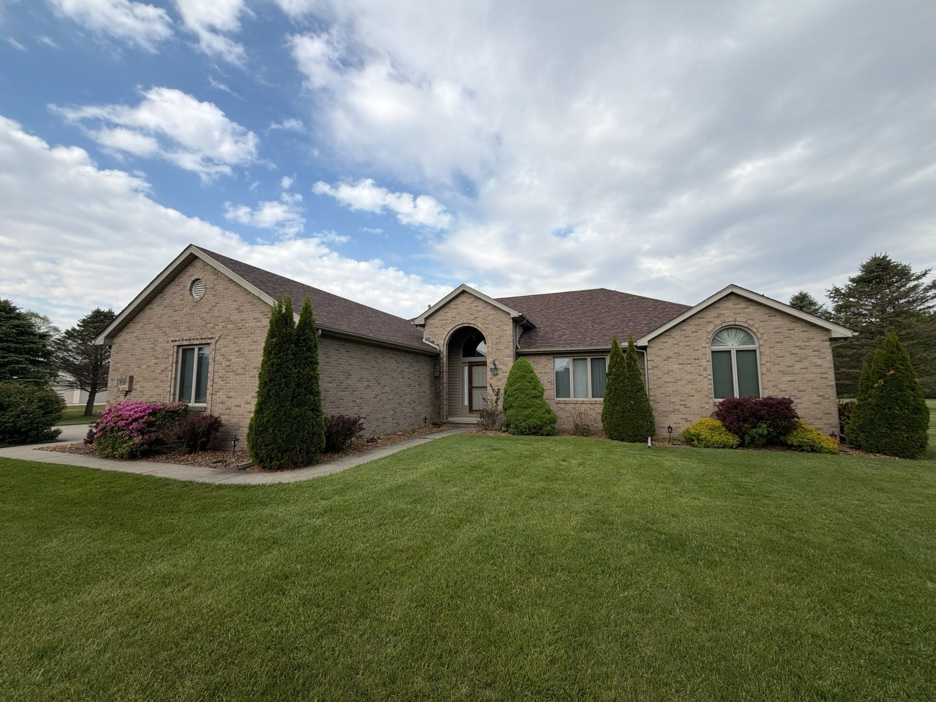 Single-story brick house with a manicured green lawn and cloudy sky