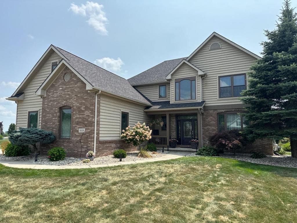 Suburban two-story brick and siding house with a front lawn and small front garden.