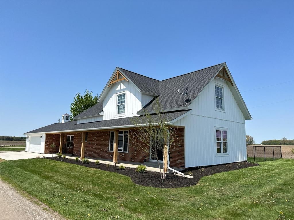 White farmhouse with a covered porch and dark roof on a grassy lot under a clear blue sky