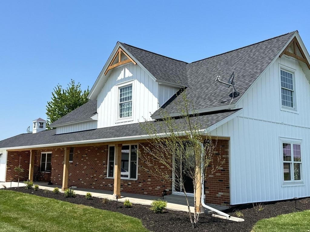 White two-story house with brick and white siding, dark roof, and a front porch under a blue sky