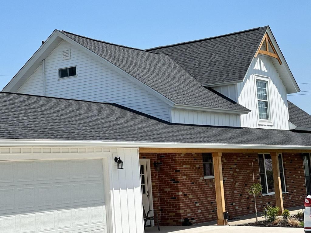 Suburban house with gray roof, white siding, brick porch, and attached garage under a clear sky