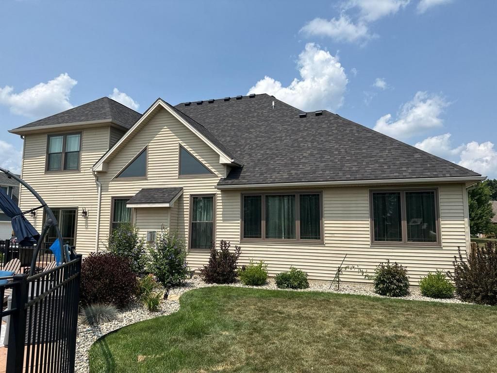 Suburban beige house with dark gray roof, front lawn, and blue sky with clouds