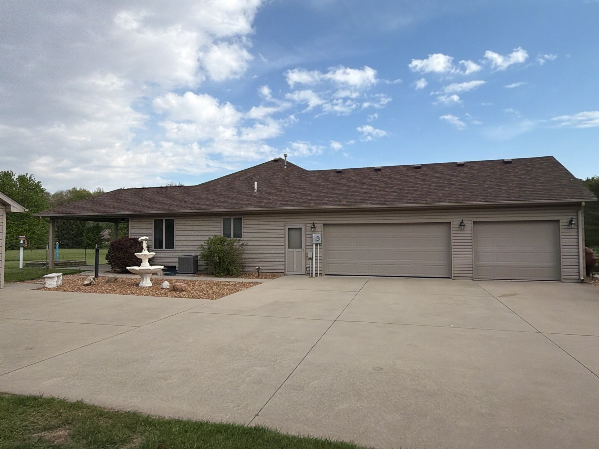 Suburban single-story house with three-car garage, concrete driveway, and blue sky with clouds