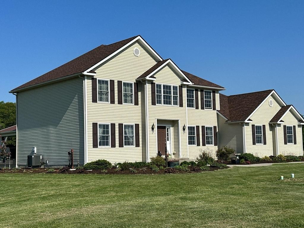 Suburban two-story cream house with dark roof and green lawn under a clear blue sky