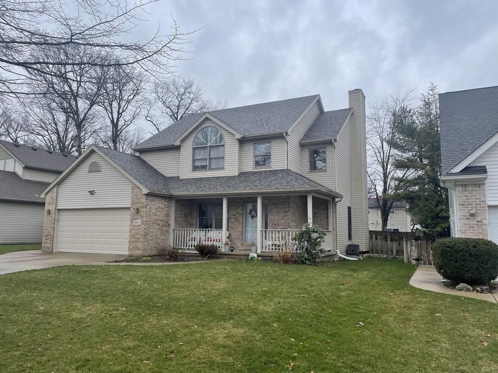 Suburban two-story house with gray siding, front porch, and attached garage behind a green lawn