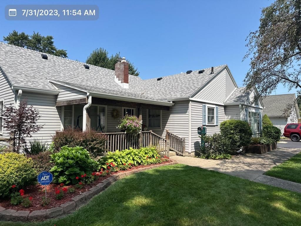 Suburban house with white siding, stone facade, front garden, and driveway under a blue sky