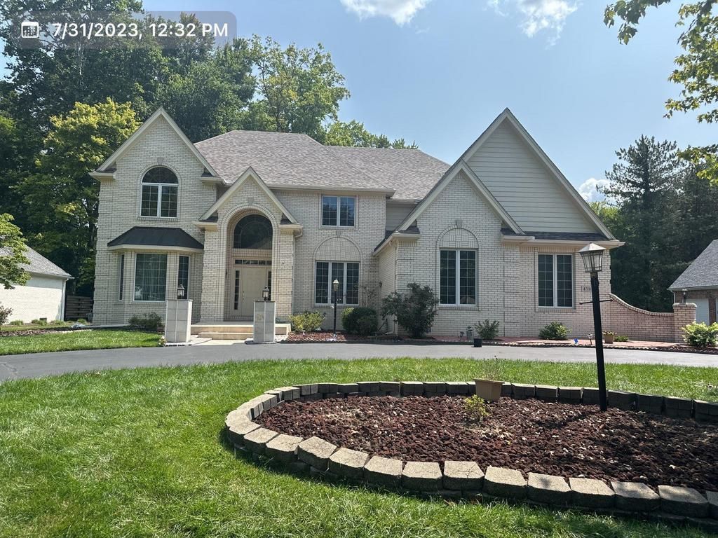 Suburban stone-and-siding house with landscaped front yard and circular flower bed under a sunny sky