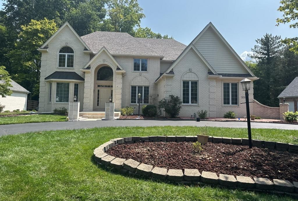 Suburban house with stone facade, arched entry, and landscaped front yard under a clear sky