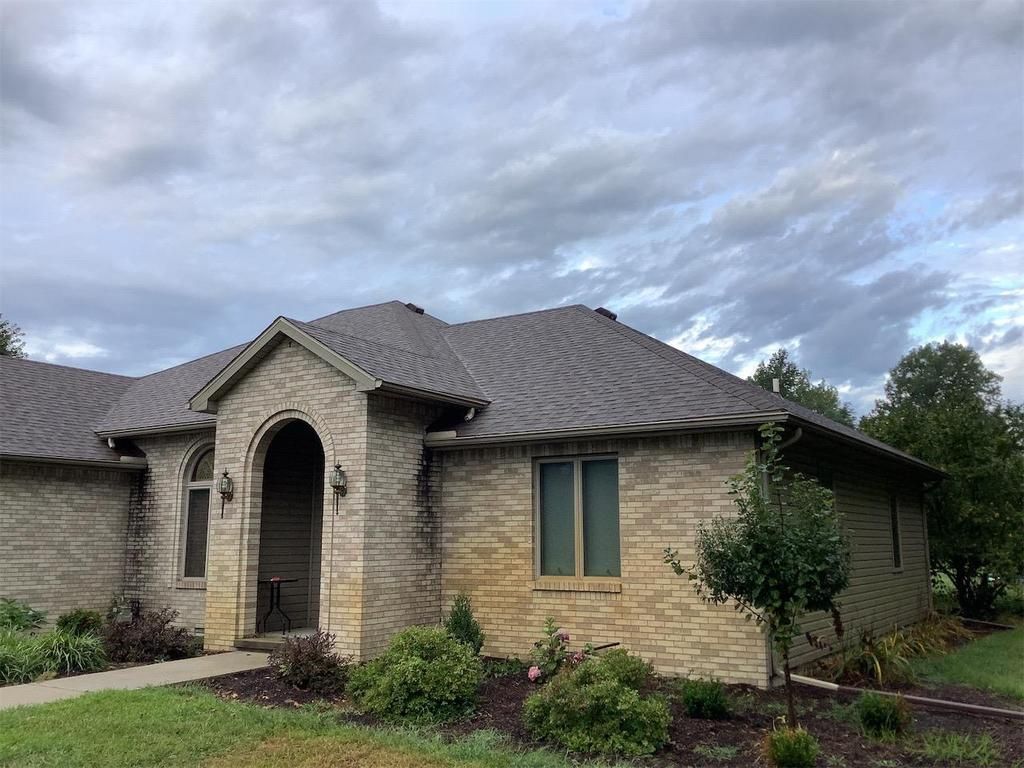 Single-story brick house with arched entry, dark shingle roof, and cloudy sky above