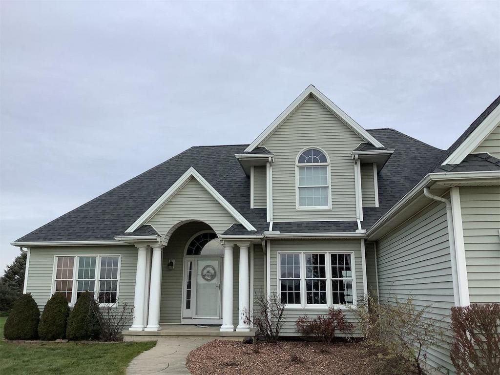 Suburban house with light siding, dark roof, front porch, and arched dormer windows
