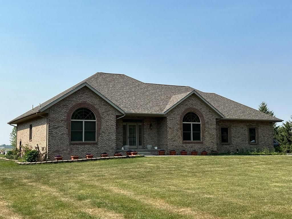 Single-story brick house with arched windows on a grassy hill under a clear blue sky
