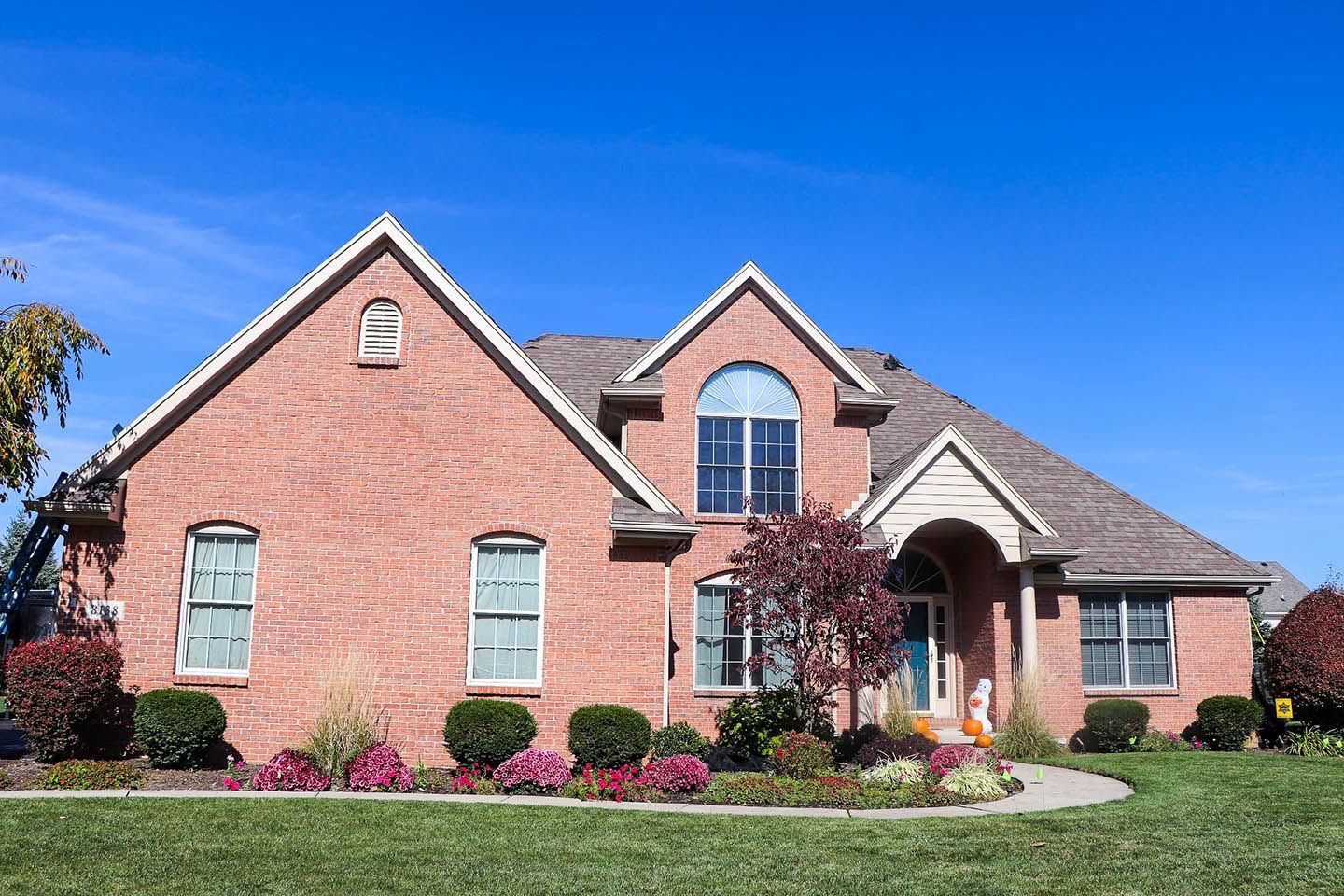 Brick suburban house with a manicured lawn, arched entry, and blue sky