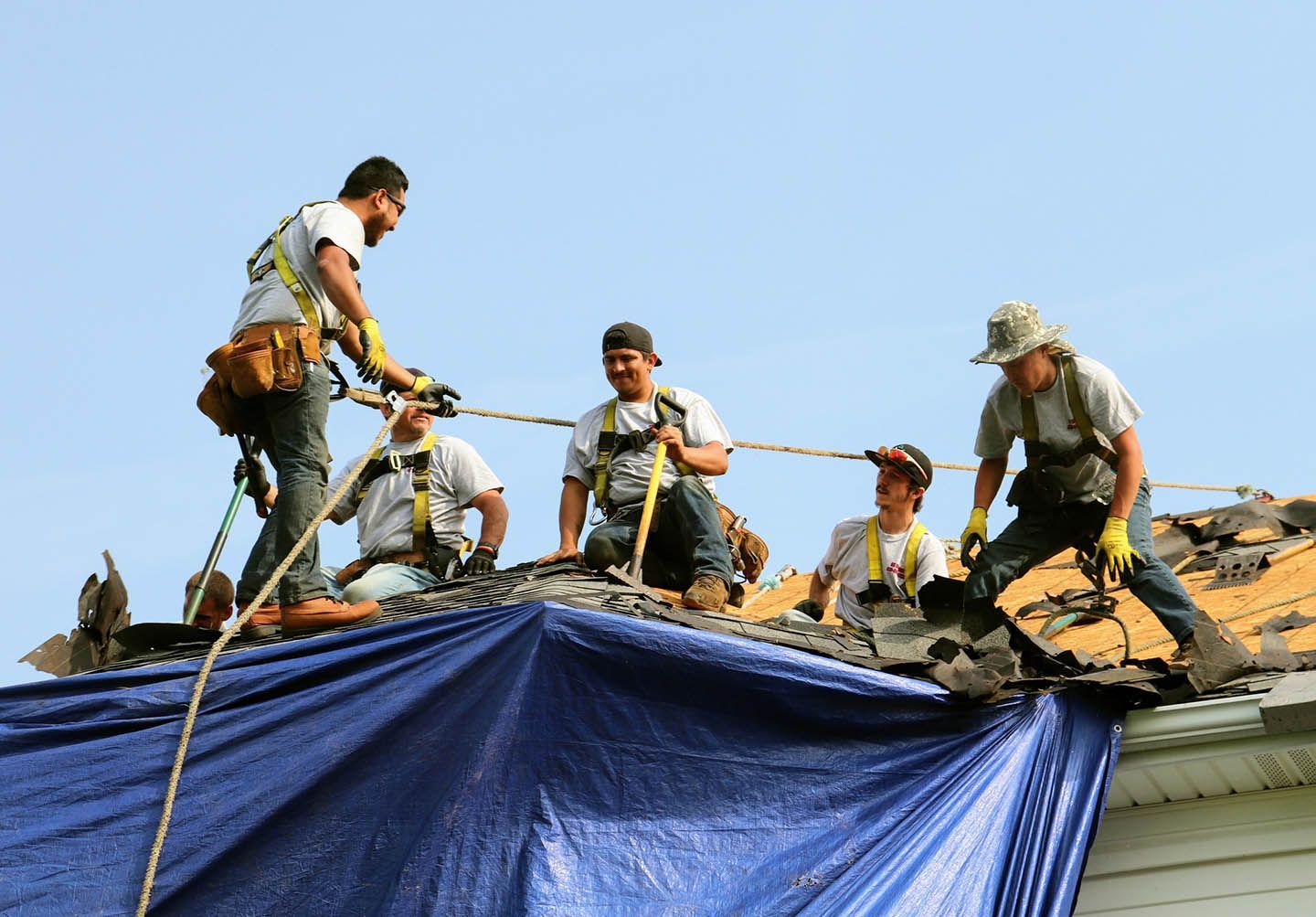 Workers securing a blue tarp on a rooftop under a clear sky