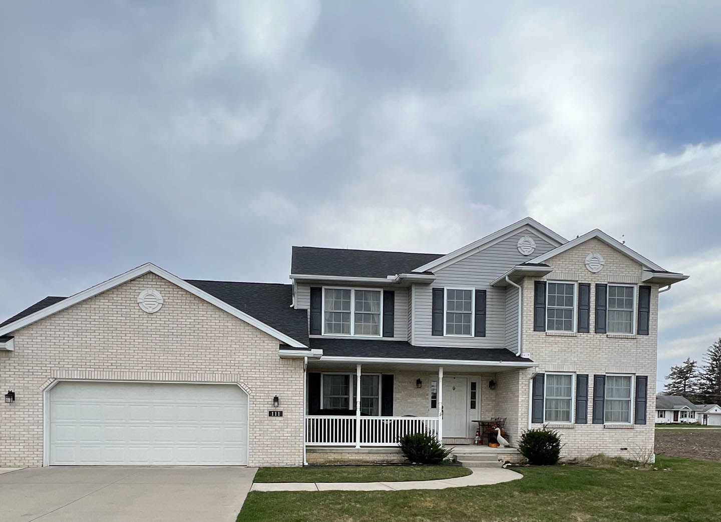 Two-story suburban house with white siding, attached garage, and covered front porch under a cloudy sky