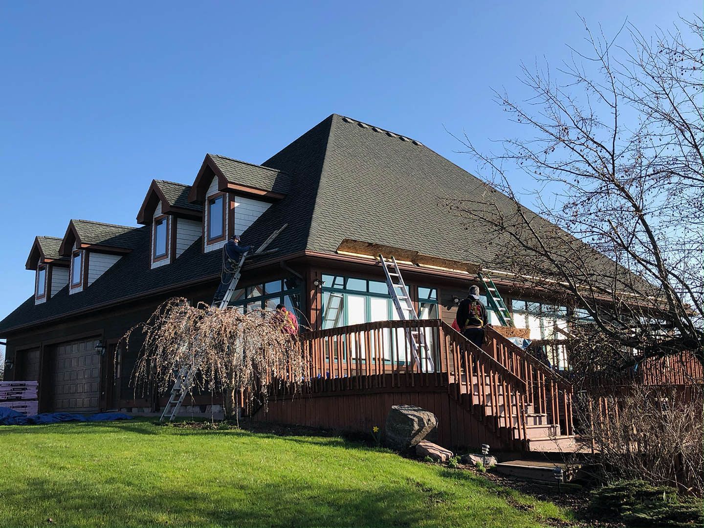 Large brick house with a steep roof, wooden deck, and green lawn on a sunny day
