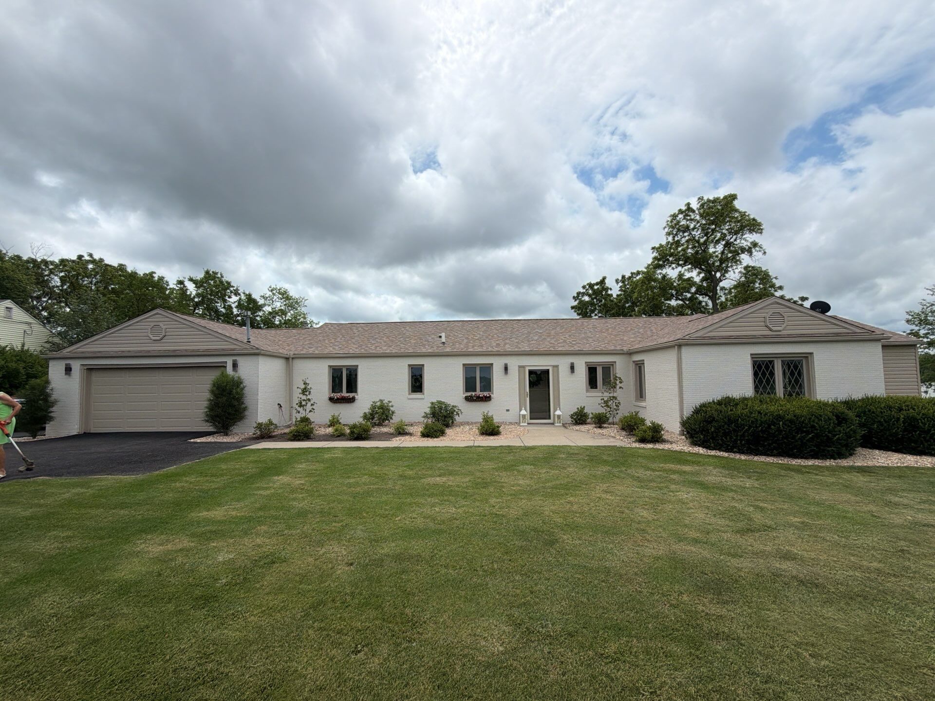 Single-story white house with gray roof, attached garage, and a front lawn under cloudy skies