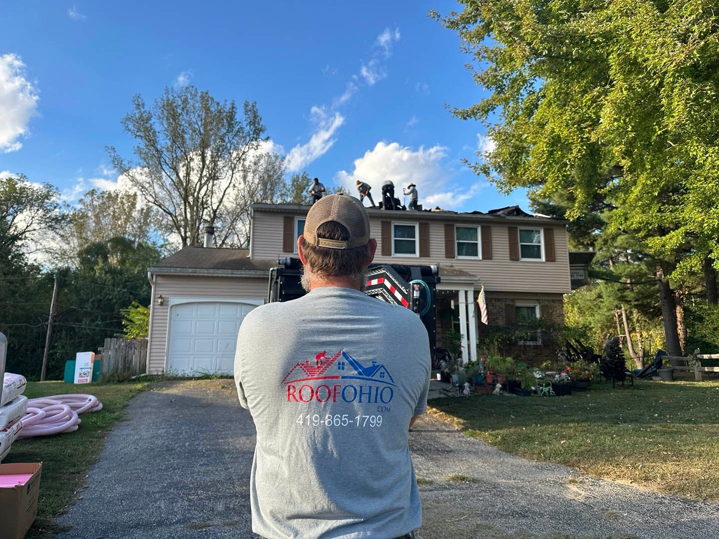 Person in gray shirt taking a photo of a house with a decorated front entrance and driveway at sunset