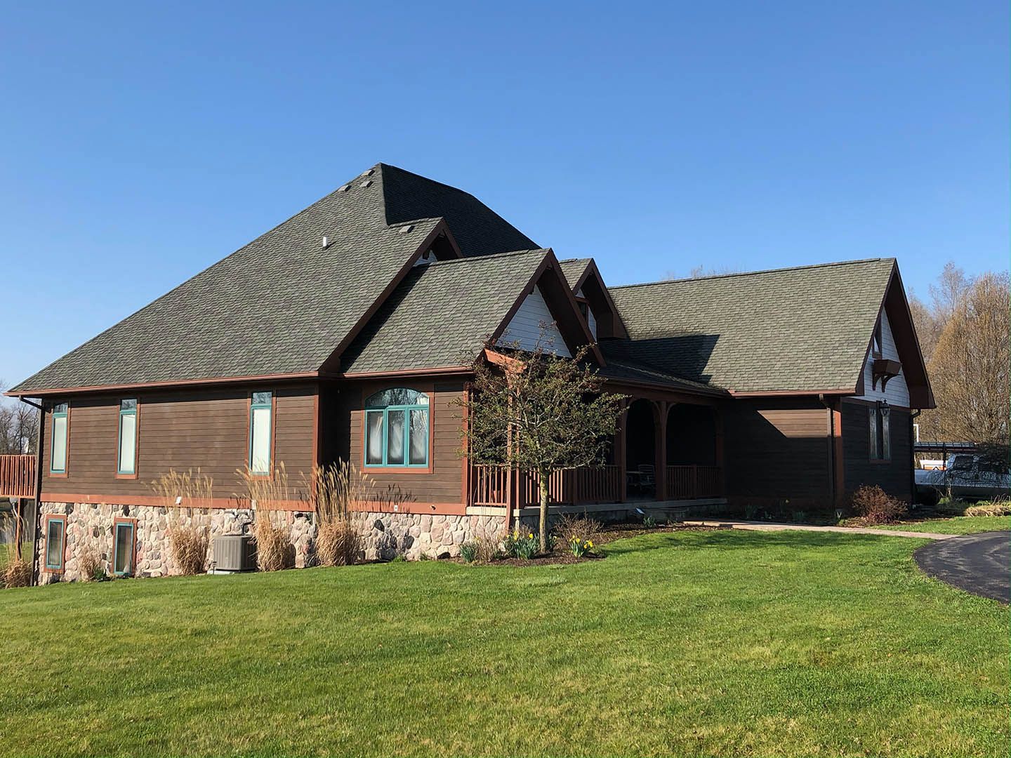 Brick house with a steep gray roof, green lawn, and clear blue sky