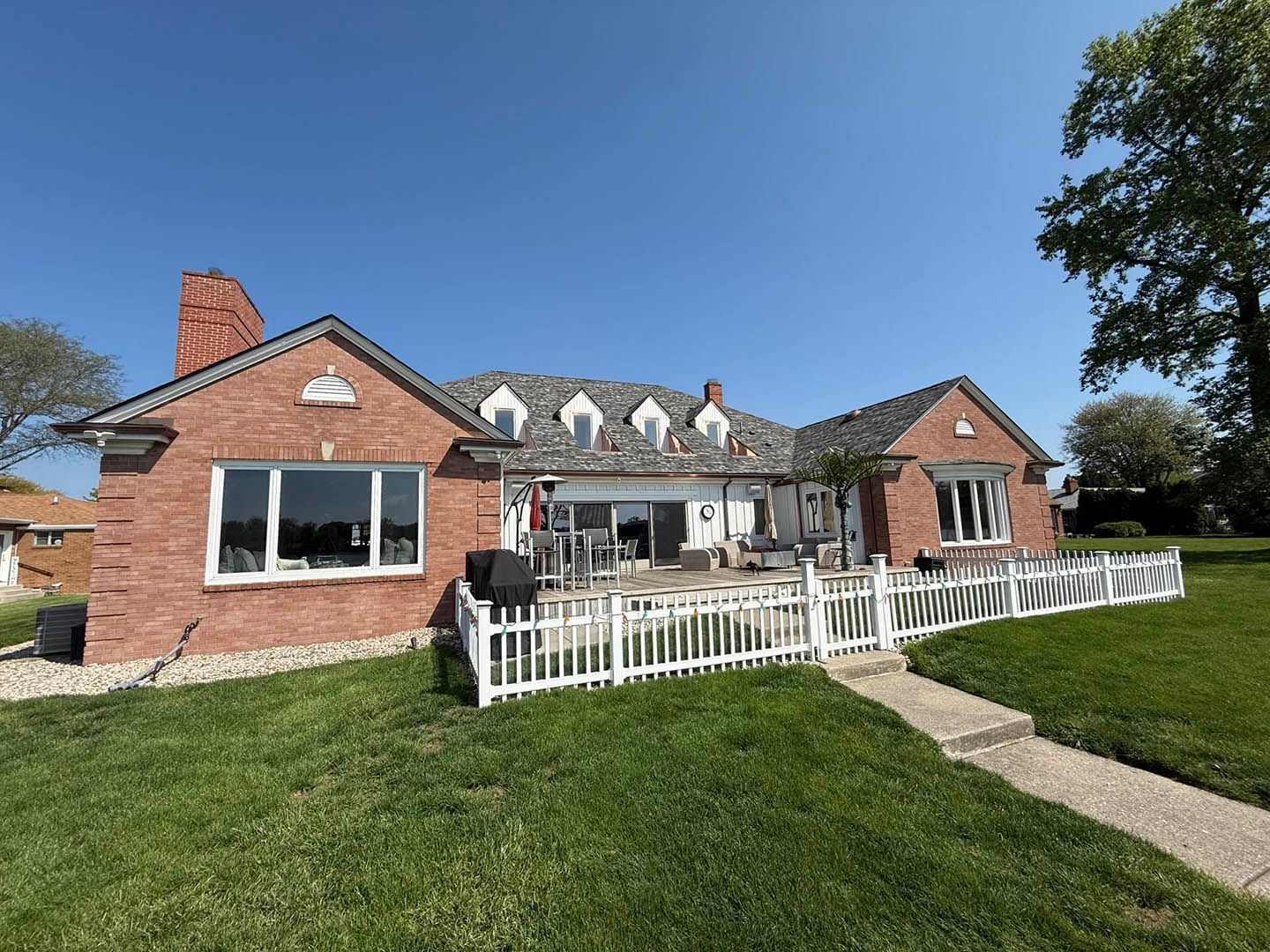 Red brick house with white fence, green lawn, and clear blue sky