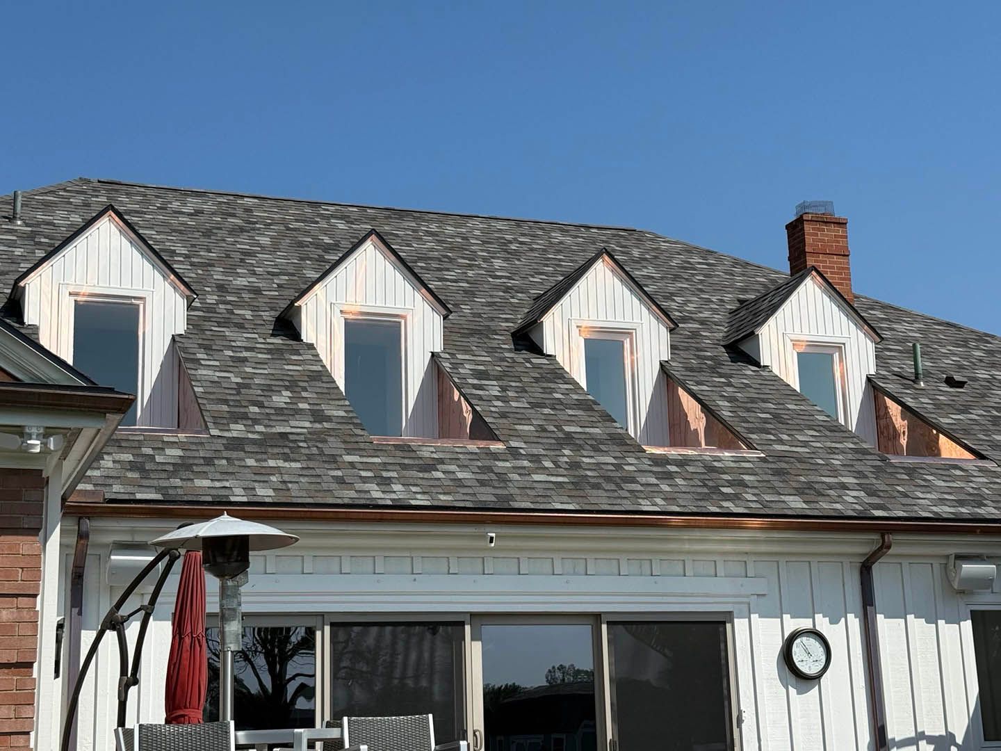 White house roof with three dormer windows and a brick chimney under a clear blue sky